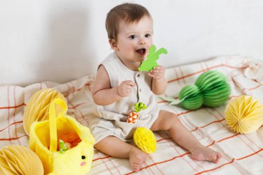 Mutlu Paskalyalar! Renkli paskalya kağıtlı yumurtaları, sepeti, şenlikli dekorasyonu ve havuçları olan şirin bir bebek. Sevimli Paskalya tavşanı ve Paskalya avı.