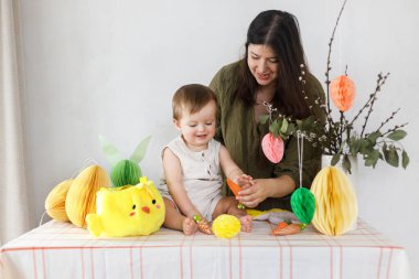 Mutlu Paskalyalar! Sevimli bebek ve mutlu anne renkli paskalya kâğıdı yumurtaları, şenlikli dekorasyon ve havuçlarla dekore ediyorlar. Sevimli Paskalya tavşanı ve Paskalya avı.