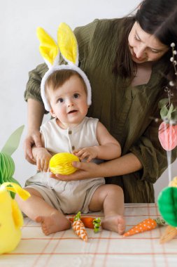 Mutlu Paskalyalar! Sevimli bebek ve mutlu anne renkli paskalya kâğıdı yumurtaları, şenlikli dekorasyon ve havuçlarla dekore ediyorlar. Sevimli Paskalya tavşanı ve Paskalya avı.