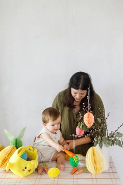 Mutlu Paskalyalar! Sevimli bebek ve mutlu anne renkli paskalya kâğıdı yumurtaları, şenlikli dekorasyon ve havuçlarla dekore ediyorlar. Sevimli Paskalya tavşanı ve Paskalya avı.