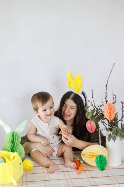 Mutlu Paskalyalar! Sevimli bebek ve mutlu anne renkli paskalya kâğıdı yumurtaları, şenlikli dekorasyon ve havuçlarla birlikte oynuyorlar. Sevimli Paskalya tavşanı ve Paskalya avı.