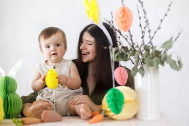 Mutlu Paskalyalar! Sevimli bebek ve mutlu anne renkli paskalya kâğıdı yumurtaları, şenlikli dekorasyon ve havuçlarla birlikte oynuyorlar. Sevimli Paskalya tavşanı ve Paskalya avı.