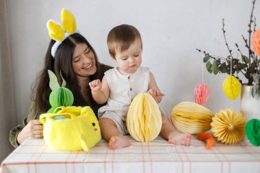 Mutlu Paskalyalar! Sevimli bebek ve mutlu anne renkli paskalya kâğıdı yumurtaları, şenlikli dekorasyon ve havuçlarla birlikte oynuyorlar. Sevimli Paskalya tavşanı ve Paskalya avı.