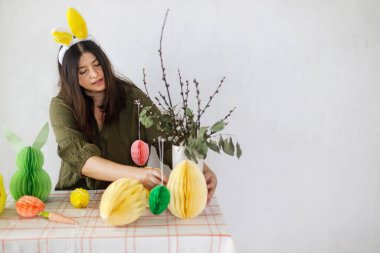 Mutlu Paskalyalar! Tavşan kulaklı şık bir kadın renkli paskalya yumurtaları, tavşanlar ve havuçlarla süslüyor. Paskalya sofrası kurma ve Paskalya avı.