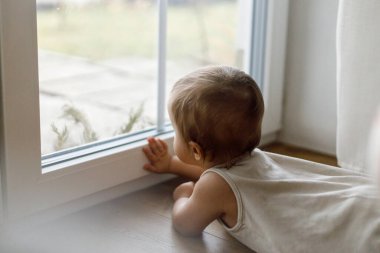 Pencerede sevimli bir bebek var. Yaklaş. Pencere camlarıyla oynayan sevimli bir bebek. Bebek aktivitesi ve bebek koruması.