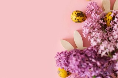 Mutlu Paskalyalar! Modern sarı yumurtalar, tavşan kulakları ve leylak çiçekleri pembe arkaplanda yazı için yer açıyordu. Paskalya bayrağı, poster şablonu