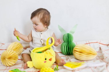 Mutlu Paskalyalar! Renkli paskalya kağıtlı yumurtaları, sepeti, şenlikli dekorasyonu ve havuçları olan şirin bir bebek. Sevimli Paskalya tavşanı ve Paskalya avı.