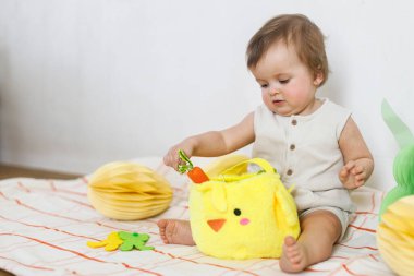 Paskalya bebeğinin paskalya sepetindeki renkli yumurta ve havuçlarla oynaması. Sevimli Paskalya tavşanı ve Paskalya avı konsepti. Mutlu Paskalyalar