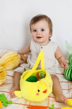 Mutlu Paskalyalar! Renkli paskalya kağıtlı yumurtaları, sepeti, şenlikli dekorasyonu ve havuçları olan şirin bir bebek. Sevimli Paskalya tavşanı ve Paskalya avı.