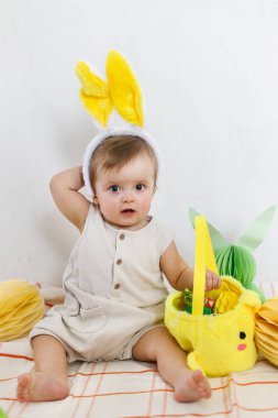 Renkli yumurtalar ve sepetten çıkan havuçlarla oynayan tavşan kulaklı şık bir Paskalya bebeği. Sevimli Paskalya tavşanı ve Paskalya avı konsepti. Mutlu Paskalyalar