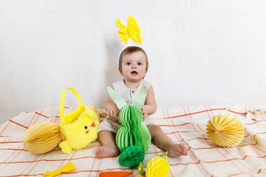 Renkli yumurtalar ve sepetten çıkan havuçlarla oynayan tavşan kulaklı şık bir Paskalya bebeği. Sevimli Paskalya tavşanı ve Paskalya avı konsepti. Mutlu Paskalyalar