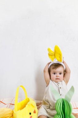 Renkli yumurtalar ve sepetten çıkan havuçlarla oynayan tavşan kulaklı şık bir Paskalya bebeği. Sevimli komik Paskalya tavşanı ve Paskalya avı konsepti. Mutlu Paskalyalar