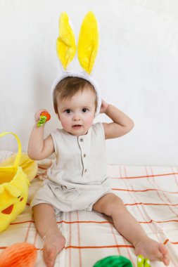 Renkli yumurtalar ve sepetten çıkan havuçlarla oynayan tavşan kulaklı şık bir Paskalya bebeği. Sevimli Paskalya tavşanı ve Paskalya avı konsepti. Mutlu Paskalyalar