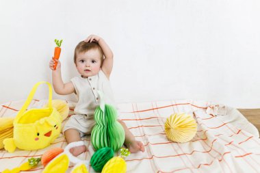 Mutlu Paskalyalar! Renkli paskalya kağıtlı yumurtaları, sepeti, şenlikli dekorasyonu ve havuçları olan şirin bir bebek. Sevimli Paskalya tavşanı ve Paskalya avı.