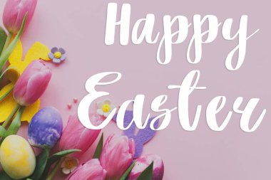 Paskalya tebrik kartı. Mutlu Paskalya metinleri ve Paskalya tarzı yumurtalar, tavşan kulakları ve çiçek açan laleler pembe arka planda yatıyordu.