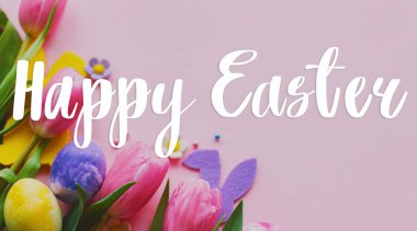 Mutlu Paskalyalar! Paskalya mesajlı tebrik kartı, paskalya yumurtaları, tavşan kulakları ve laleler pembe arka planda yatıyordu.