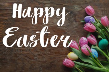 Mutlu Paskalyalar! Tebrik kartı. Mutlu Paskalya metinleri ve Paskalya tarzı yumurtalar ve çiçek açan laleler kırsal ahşap arka planda yatıyordu.