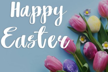 Paskalya tebrik kartı. Mutlu Paskalya metinleri ve Paskalya tarzı yumurtalar ve çiçek açan laleler mavi arka planda yatıyordu.