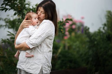 Anneler Günün kutlu olsun! Anne bahçede sevimli yeni doğmuş bebeği öpüyor ve sarılıyor. Kırsal alanda sevgi, ilgi ve aile. Evlat edinme ve annelik