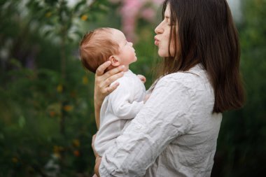 Anneler Günün kutlu olsun! Anne bahçede sevimli yeni doğmuş bebeği öpüyor ve sarılıyor. Kırsal alanda sevgi, ilgi ve aile. Evlat edinme ve annelik