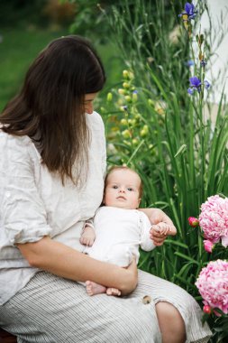 Anneler Günün kutlu olsun! Anne bahçede çiçeklerin arasında sevimli yeni doğmuş bebeğe sarılıyor. Kırsal alanda sevgi, ilgi ve aile. Evlat edinme ve annelik