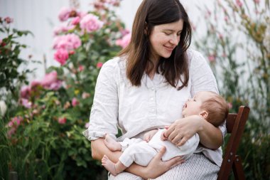 Anneler Günün kutlu olsun! Anne bahçede çiçeklerin arasında sevimli yeni doğmuş bebeğe sarılıyor. Kırsal alanda sevgi, ilgi ve aile. Evlat edinme ve annelik