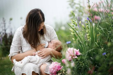Anneler Günün kutlu olsun! Anne, bahçede bir şişeyle sevimli bir bebeği kucaklıyor ve besliyordu. Kırsal alanda sevgi, ilgi ve aile. Evlat edinme ve annelik