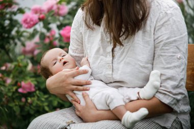Anneler Günün kutlu olsun! Anne bahçede çiçeklerin arasında sevimli yeni doğmuş bebeğe sarılıyor. Kırsal alanda sevgi, ilgi ve aile. Evlat edinme ve annelik