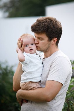 Genç baba yaz bahçesinde yeni doğmuş bebeğe sarılıyor. Baba oğluna sarılıyor ve tatlı bebeği dışarıda öpüyor. Babalar günün kutlu olsun! Evlat edinme, aşk ve aile kavramı