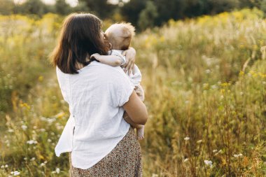 Mutlu anne, yeni doğmuş bebeği akşamları çayırda tutuyor. Aşk ve aile kavramı. Anne ve tatlı oğlu tarlada yürüyor. Anneler günün kutlu olsun.!