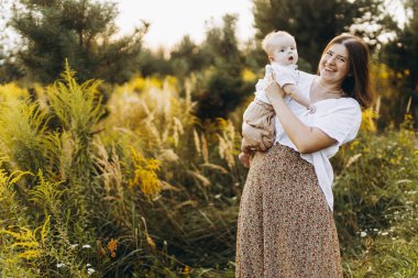 Mutlu anne, yeni doğmuş bebeği akşamları çayırda tutuyor. Aşk ve aile kavramı. Anne ve tatlı oğlu tarlada yürüyor. Anneler günün kutlu olsun.!