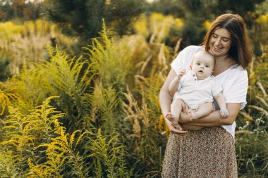 Mutlu anne, yeni doğmuş bebeği akşamları çayırda tutuyor. Aşk ve aile kavramı. Anne ve tatlı oğlu tarlada yürüyor. Anneler günün kutlu olsun.!