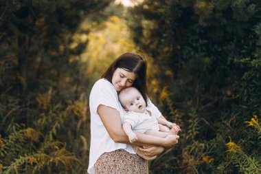 Mutlu anne, yeni doğmuş bebeğini akşam çayırda kucaklıyor. Aşk, ilgi ve aile kavramı. Anne ve tatlı oğlu tarlada dinleniyor. Anneler günün kutlu olsun.!