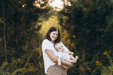 Mutlu anne, yeni doğmuş bebeğini akşam çayırda kucaklıyor. Aşk, ilgi ve aile kavramı. Anne ve tatlı oğlu tarlada dinleniyor. Anneler günün kutlu olsun.!
