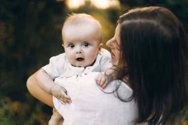 Mutlu anne, yeni doğmuş bebeğini akşam çayırda kucaklıyor. Aşk, ilgi ve aile kavramı. Anne ve tatlı oğlu tarlada dinleniyor. Anneler günün kutlu olsun.!