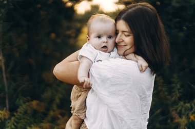 Mutlu anne, yeni doğmuş bebeğini akşam çayırda kucaklıyor. Aşk, ilgi ve aile kavramı. Anne ve tatlı oğlu tarlada dinleniyor. Anneler günün kutlu olsun.!