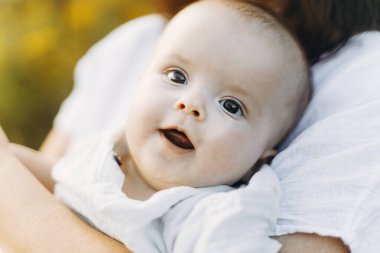Annesinin ellerinde mutlu bir bebeğin portresi. Anne, akşam vakti küçük bebeğe çayırda sarılıyor. Aşk, ilgi ve koruma konsepti. Anne ve oğlu. Anneler günün kutlu olsun.!