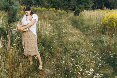 Mutlu anne, yeni doğmuş bebeği akşamları çayırda tutuyor. Aşk ve aile kavramı. Anne ve tatlı oğlu tarlada yürüyor. Anneler günün kutlu olsun.!