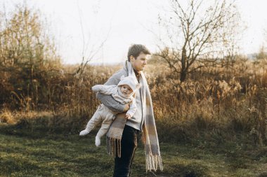 Mutlu bir baba, güz tarlasında, yumuşak bir akşam ışığında tatlı oğluyla sarılıp eğleniyor. Ebeveynlik. Baba ve küçük çocuk rahat kıyafetler içinde sonbahar parkında yürüyorlar.