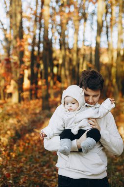 Mutlu bir baba, güz ormanında yumuşak bir akşam ışığında küçük oğluna sarılıp onu öpüyor. Babalık. Güz parkında kucaklaşan sevimli çocuklu, sıcak kazaklı şık bir adam.