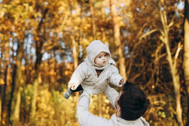 Mutlu baba, sonbahar ormanlarında yumuşak akşam ışığında tatlı oğluyla oynuyor. Babalık. Hoş çocuklu şık bir adam sıcak kazaklar içinde sonbahar parkında eğleniyor.