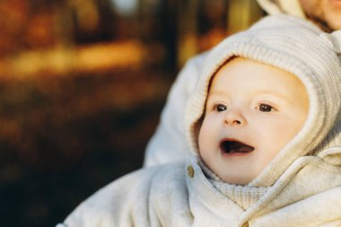 Sonbahar ormanlarında, yumuşak bir akşam ışığında babasının ellerinde gülümseyen mutlu, sevimli bir oğlan. Babalık. Sevimli çocuklu şık bir adam sıcak kazaklar içinde sonbahar parkında sarılıyor ve sarılıyor.