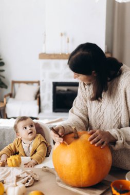 Mutlu anne ve tatlı oğlu, masasında hayaletler, örümcekler ve yarasalarla balkabağı tutuyor. Cadılar Bayramı için balkabağı oyma, balkabağı feneri yapma. Cadılar Bayramı hazırlığı