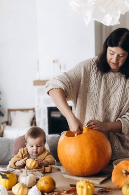 Mutlu anne ve tatlı oğlu masalara hayaletler, örümcekler ve yarasalarla balkabağı oyuyor. Cadılar bayramı balkabağı kesimi, balkabağı feneri yapmak. Cadılar Bayramı hazırlığı