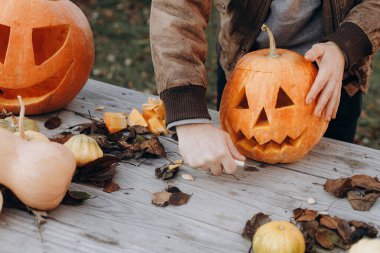 Sonbahar bahçesindeki ahşap masaya cadılar bayramı balkabağı oyan adam elleri kapalı. Sonbahar hasadı. Balkabağı kesmek, balkabağı feneri yapmak. Cadılar Bayramı hazırlığı