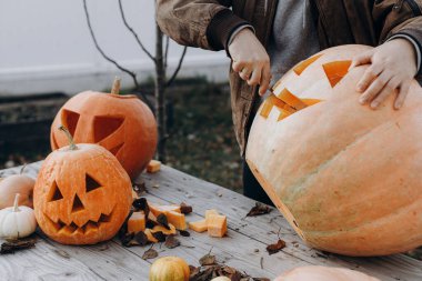 Sonbahar bahçesindeki ahşap masaya cadılar bayramı balkabağı oyan adam elleri kapalı. Sonbahar hasadı. Balkabağı kesmek, balkabağı feneri yapmak. Cadılar Bayramı hazırlığı