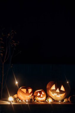 Karanlık sonbahar gecesinde kırsal ahşap masada fenerlerin üzerinde parlayan ürkütücü Jack o fenerleri. Mutlu Cadılar Bayramı! Korkunç atmosferik cadılar bayramı akşam bahçesinde oyulmuş balkabakları. Yuh! Şeker mi şaka mı? Boşluğu kopyala