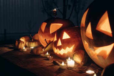 Karanlık sonbahar gecesinde kırsal ahşap masada fenerlerin üzerinde parlayan ürkütücü Jack o fenerleri. Mutlu Cadılar Bayramı! Korkunç atmosferik cadılar bayramı akşam bahçesinde oyulmuş balkabakları. Yuh! Şeker mi şaka mı? Boşluğu kopyala