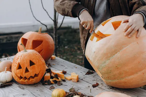 Sonbahar bahçesindeki ahşap masaya cadılar bayramı balkabağı oyan adam elleri kapalı. Sonbahar hasadı. Balkabağı kesmek, balkabağı feneri yapmak. Cadılar Bayramı hazırlığı