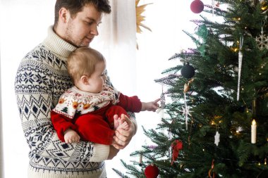 Mutlu bir baba kucağında sevimli bir oğul ve şık bir Noel ağacı tutuyor. Mutlu Noeller ve mutlu tatiller! Atmosferik aile zamanı, tatil hazırlığı.